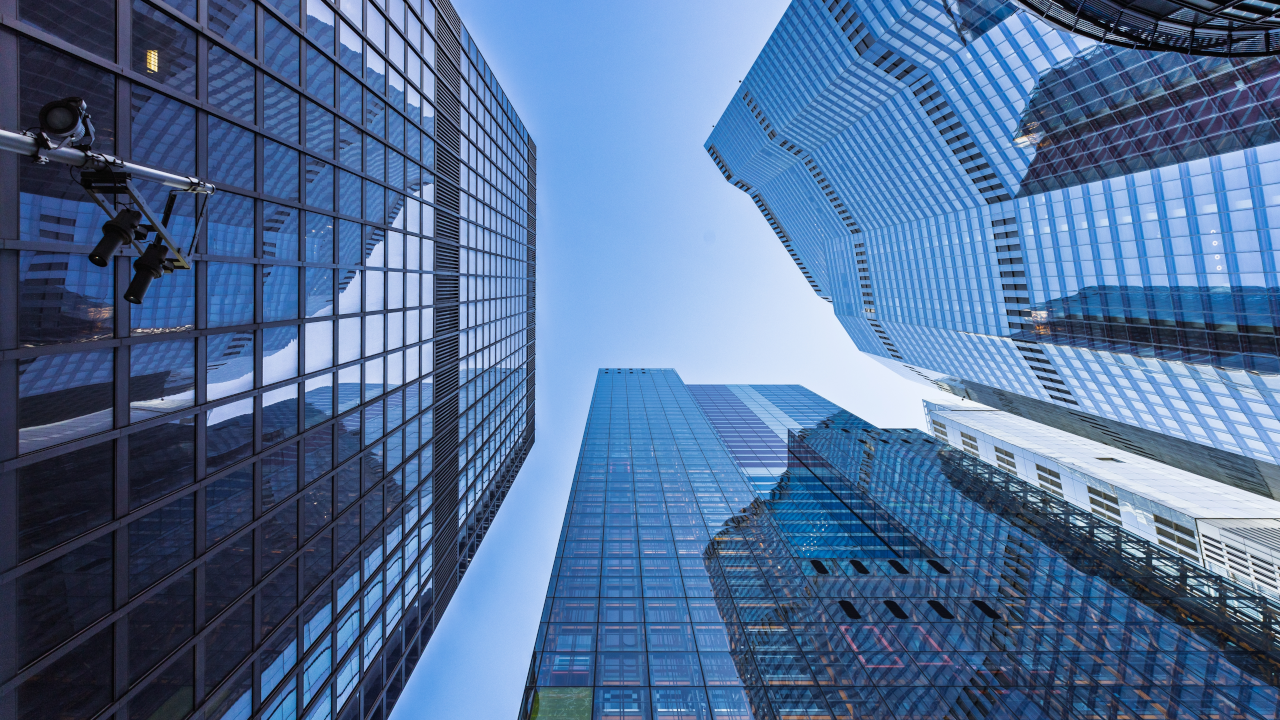 Looking up to a blue sky with three tall skyscrapers surrounding the sky.