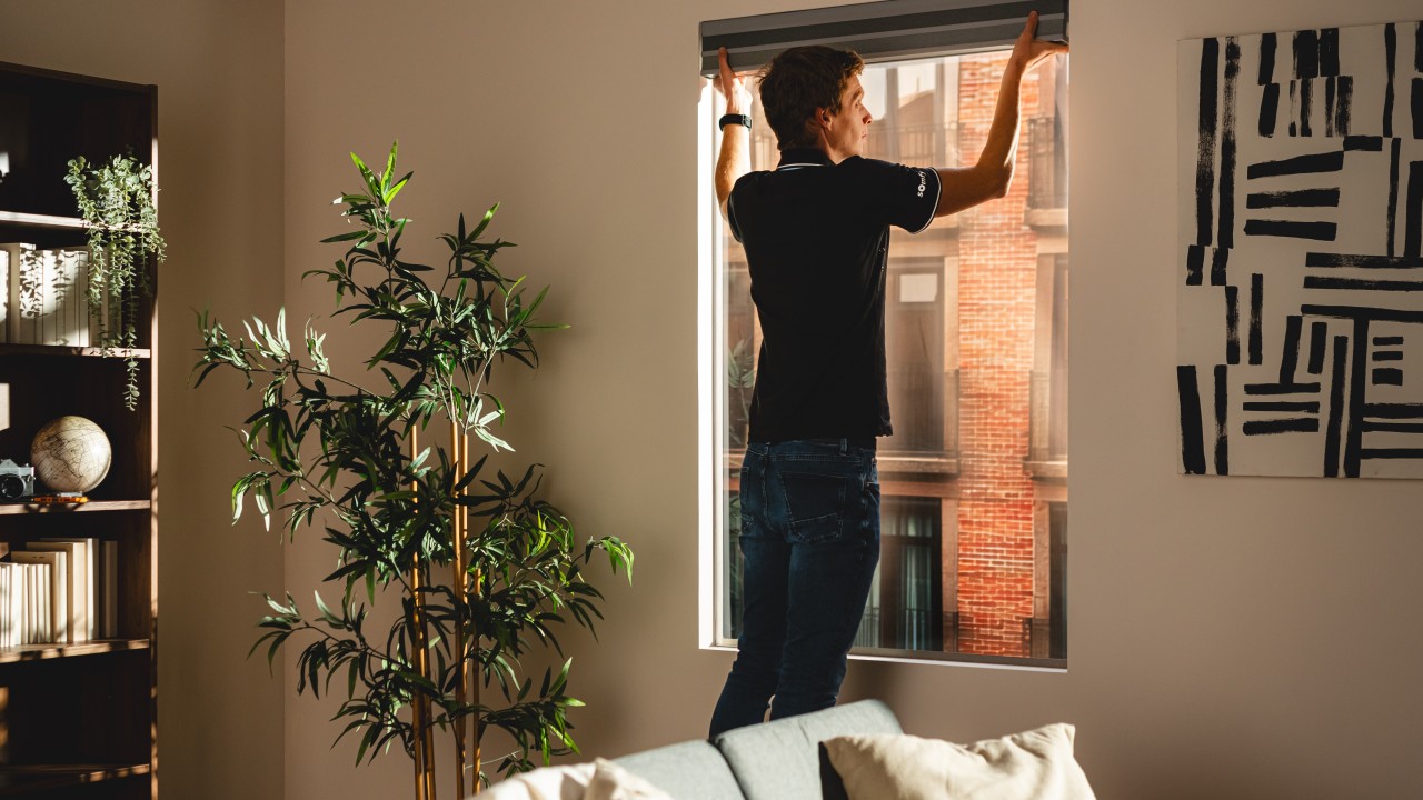 Dealer in a Somfy polo installing a motorized roller shade in a modern apartment.
